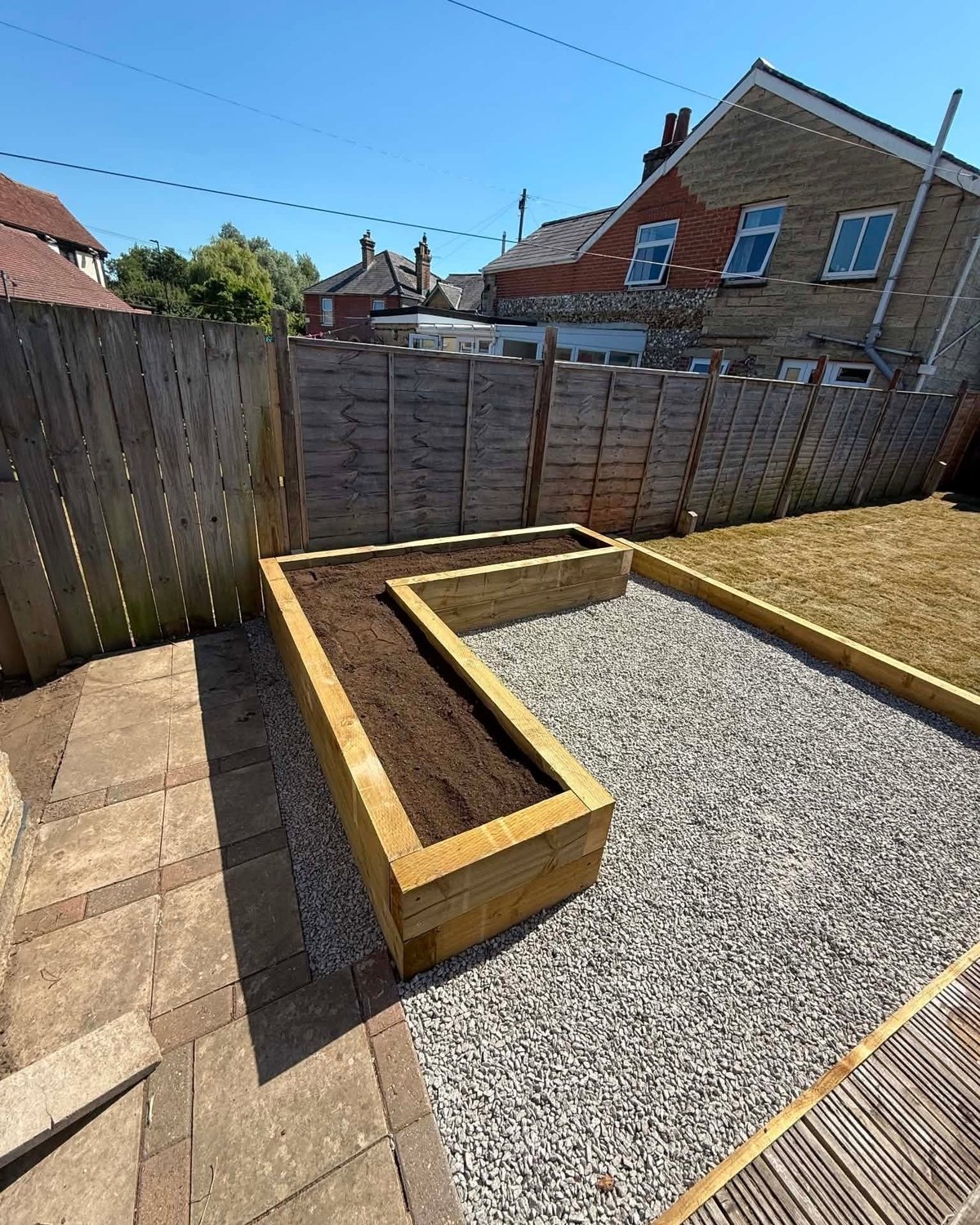 Wooden raised garden beds under construction in a backyard with gravel base and wooden fence surrounding the fenced garden area