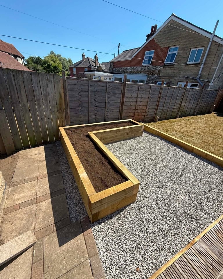 Wooden raised garden beds under construction in a backyard with gravel base and wooden fence